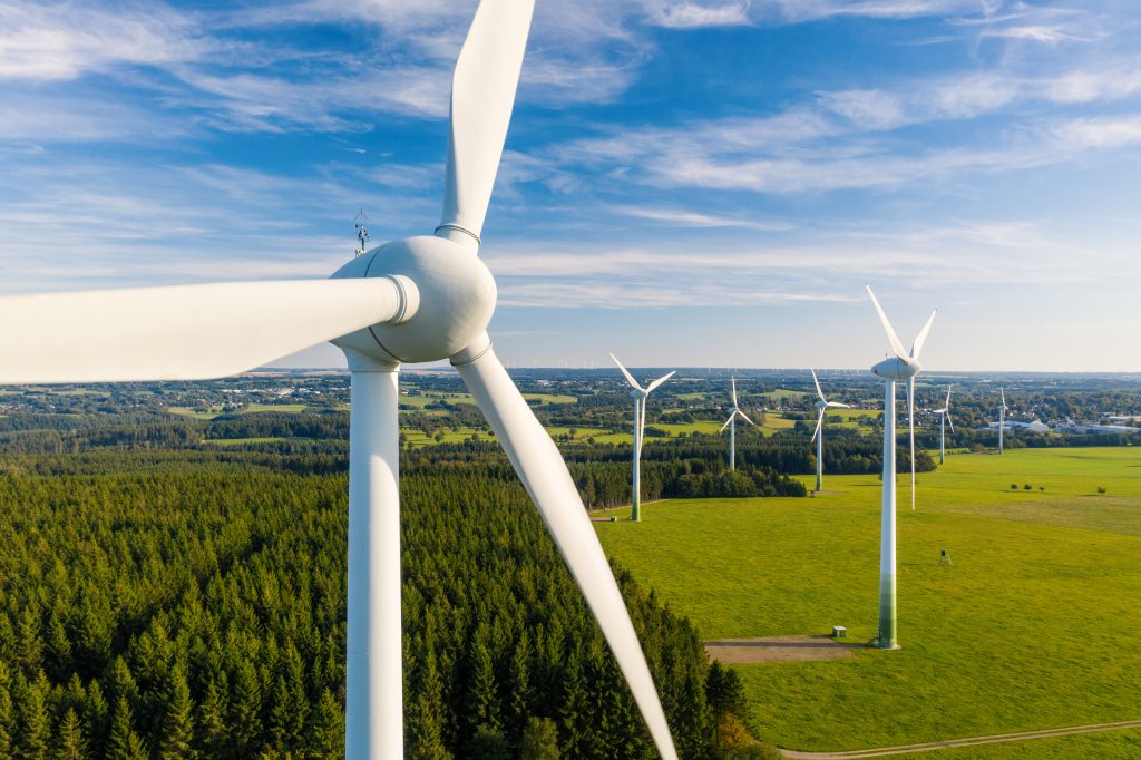 A close up of a wind turbine on an expansive field with more wind turbines visible in the background