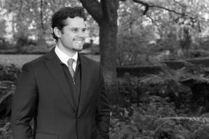 black and white professional headshot of max parylo. Max is looking off to his left and appears to be laughing.