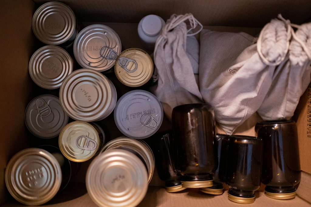 an ariel look inside a cardboard box holding tin cans, glass jars, and cloth bags on produce. the image is used to represent alternatives to packaging that contains pfas forever chemicals