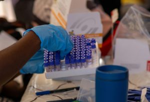 close up image of someone wearing blue hospital gloves handling a tray of test tubes used to represent healthcare in emerging markets.