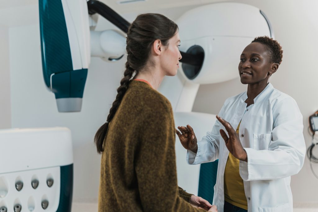 a doctor in a white lab coat speaking to her patient who is sitting on an examination table. depicting investing in healthcare, in particular women's health