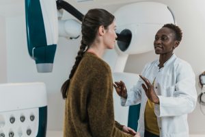a doctor in a white lab coat speaking to her patient who is sitting on an examination table. depicting investing in healthcare, in particular women's health