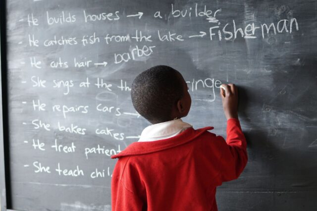young child writing on chalk board in classroom