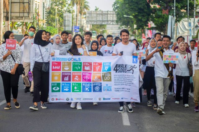 Group of people walking with a large white banner portraying the UN SDGs in Bandar Lampung, Lampung, Indonesia. Used as the feature image of a piece detailing the future of the SDGs beyond 2030 target deadlines.