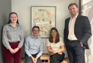 photo of Tribe's four newest employees, two on the outside standing and two in the middle sitting on a wooden bench all smiling at the camera