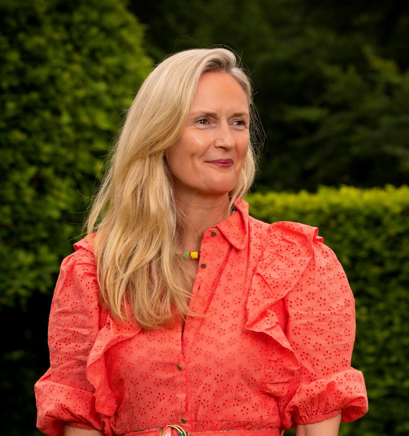 Natural headshot of Amy Clarke looking off to the right smiling, with greenery visible in the background