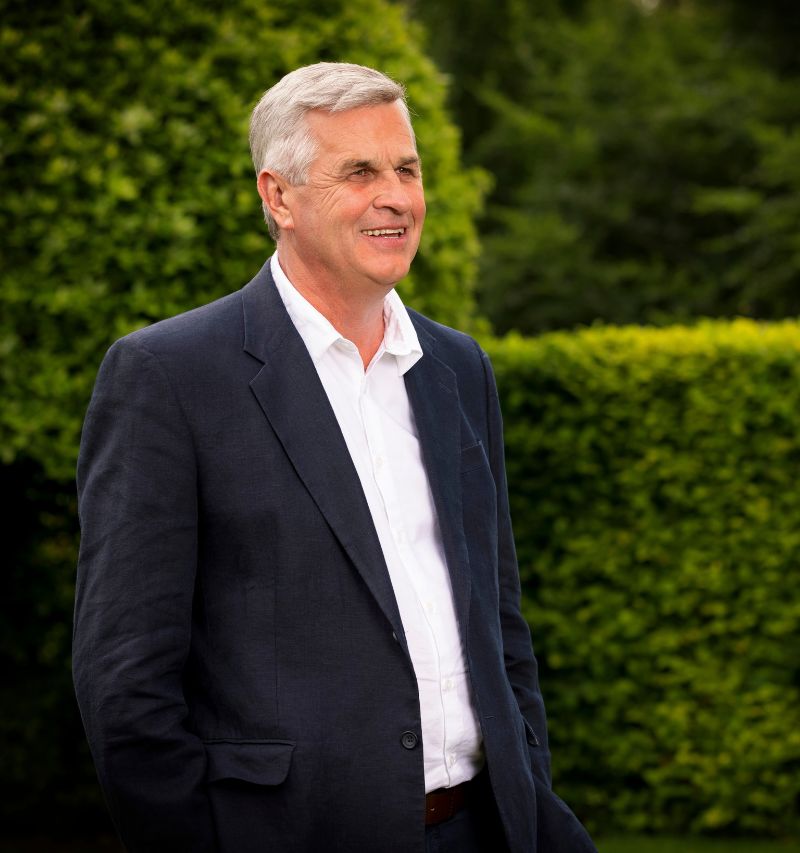 headshot of david scott naturally looking off to the side. he is outside with greenery visible in the background.
