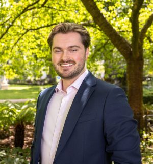Professional headshot of Callum Quinn taken in a park with greenery visible behind him.