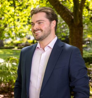natural headshot of callum quinn taken in park with greenery visible behind him. He is looking off the side smiling toward the distance.